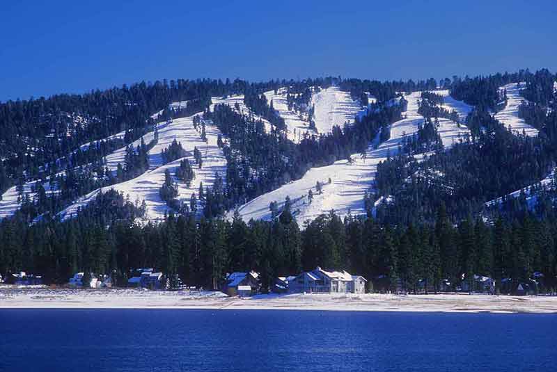 Snow-covered ski slopes form the backdrop for Big Bear, California with Big Bear Lake in the foreground.