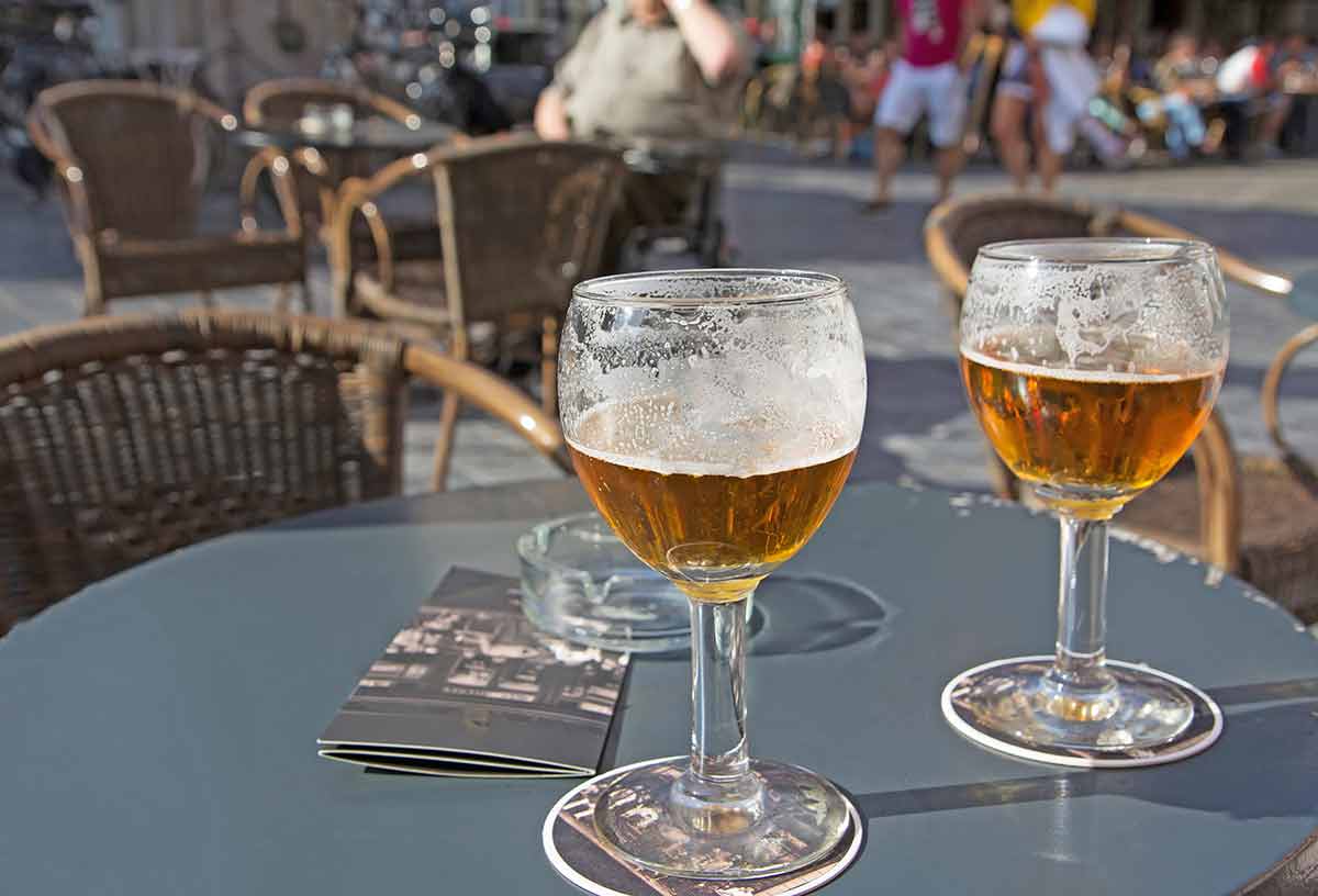 things to do in bruges brussels Close up view of two glasses of Belgian beer standing on the table on pub front garden.