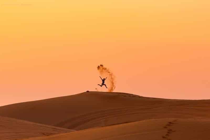 Figure of man jumping in the sand dunes in the distance in Dubai