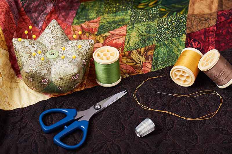 things to do in harrisonburg Spools of thread, needle, thimble, scissors and pin cushion for patchwork on a quilt.