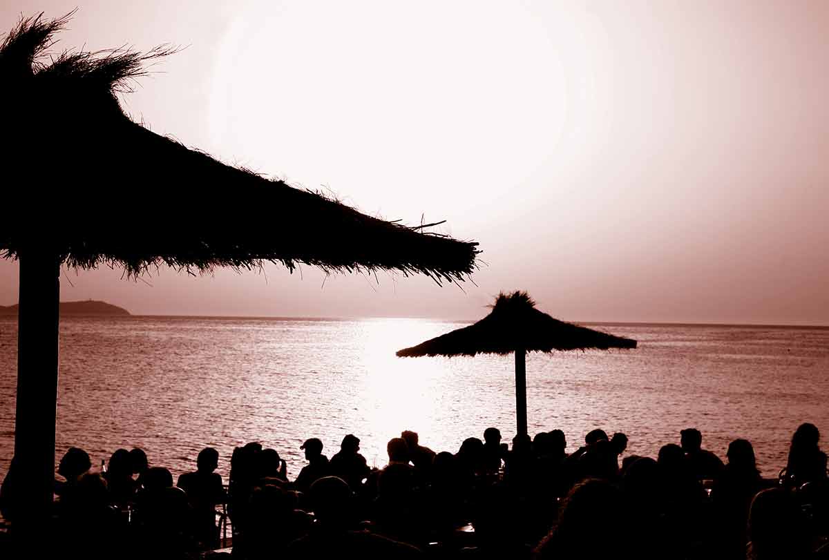 things to do in ibiza island crowd sitting under thatched umbrellas watching the sunset