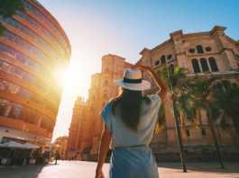 things to do in malaga Rear view of young tourist woman in white sun hat walking in Malaga city at sunset.