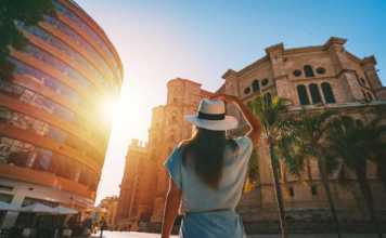 things to do in malaga Rear view of young tourist woman in white sun hat walking in Malaga city at sunset.