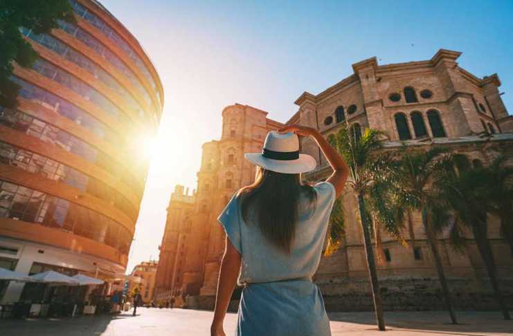 things to do in malaga Rear view of young tourist woman in white sun hat walking in Malaga city at sunset.