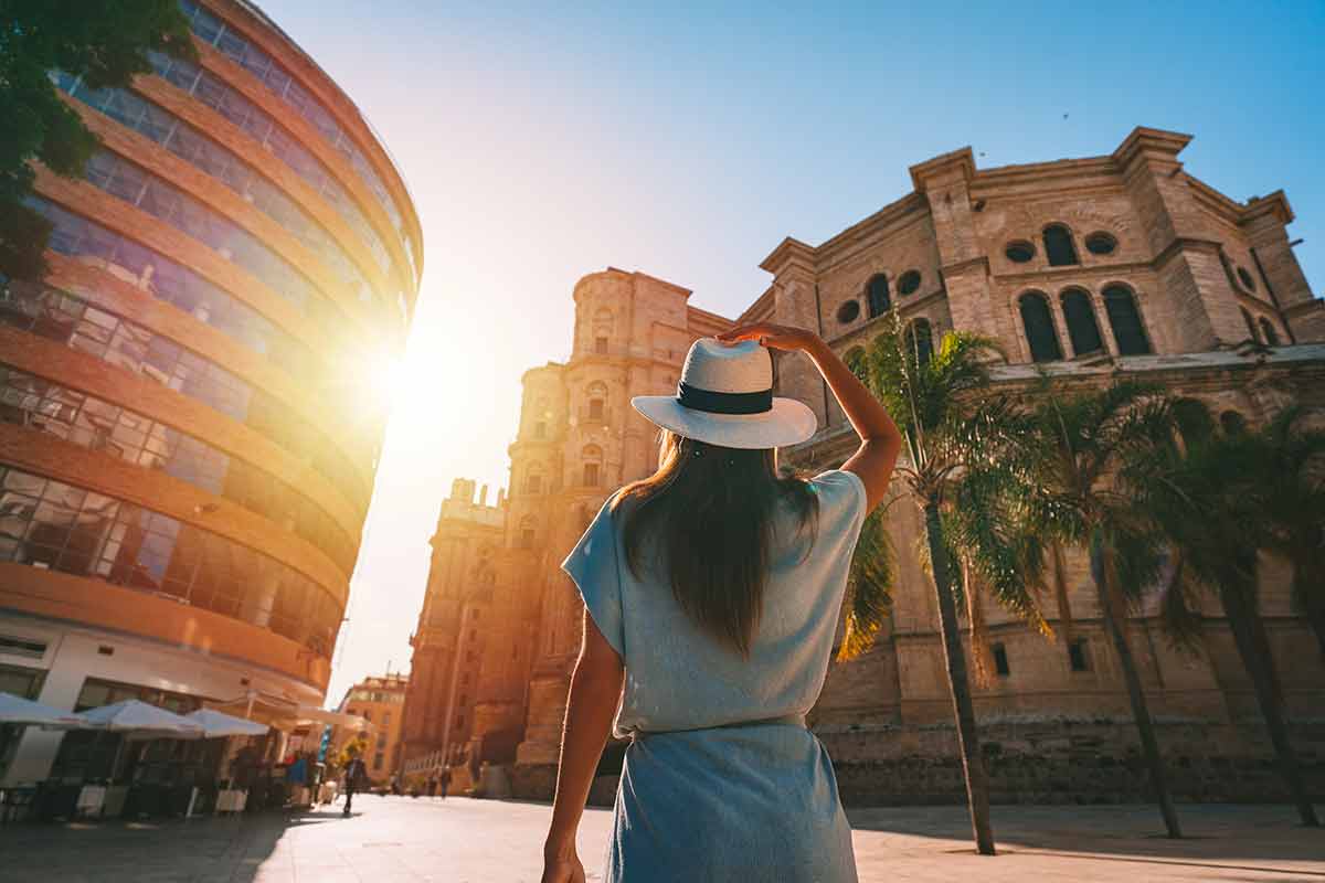 things to do in malaga Rear view of young tourist woman in white sun hat walking in Malaga city at sunset.