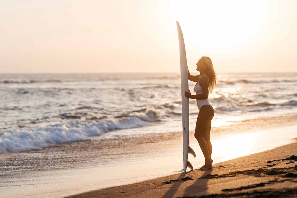 things to do in manhattan beach woman in white swimsuit holding a surf board