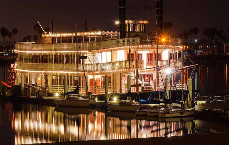 Night view of an authentic, vintage, American riverboat with two chimneys resembling the steamboats used in the 1800s on the Mississippi river.