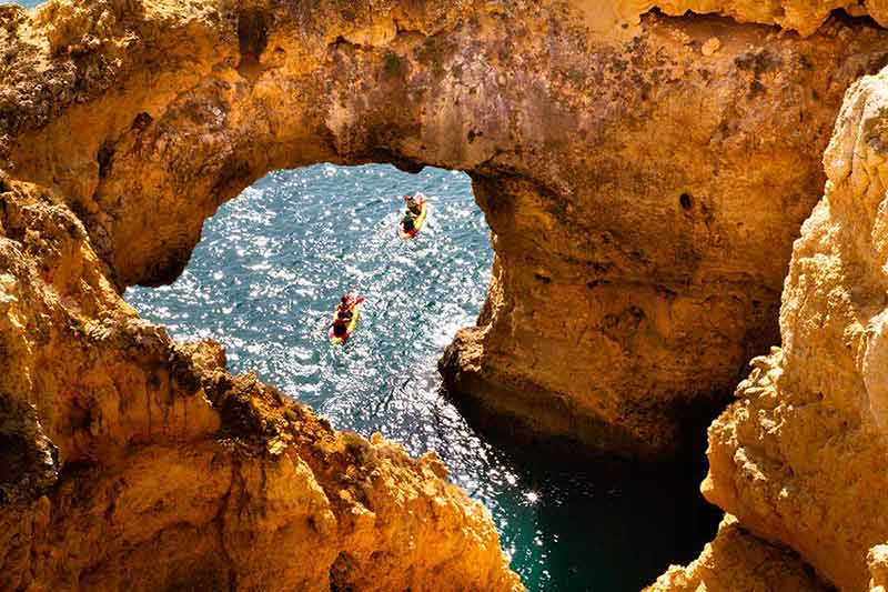 things to do in portugal algarve Two kayakers paddiling in a golden cove along the Algarve coast.
