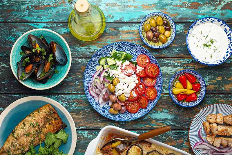 Assorted Greek dishes on rustic wooden background from above, moussaka, grilled fish, souvlaki, greek salad, steamed mussels with herbs, appetizers of Greece.