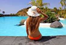 things to do in tenerife Back view girl sitting front pool with hat relaxed.