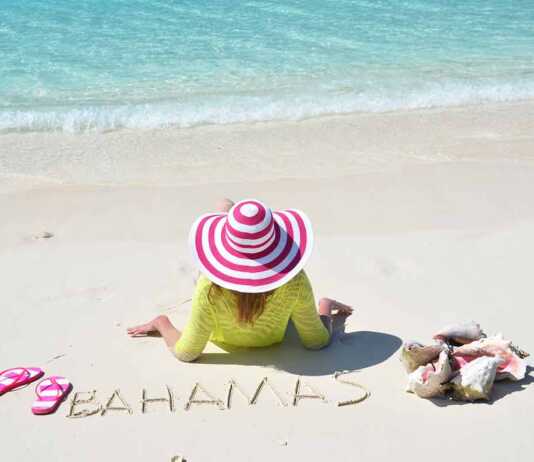 woman with a pink candy striped hat sitting on the sand in the Bahamas