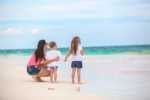 things to do with kids in cancun Rear view of fashion young mother and two her kids at exotic beach on sunny day