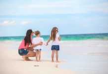 things to do with kids in cancun Rear view of fashion young mother and two her kids at exotic beach on sunny day