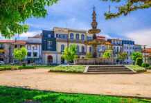 Fountain In Small Park And Typical Colorful Buildings Houses