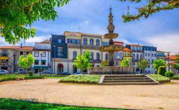 Fountain In Small Park And Typical Colorful Buildings Houses