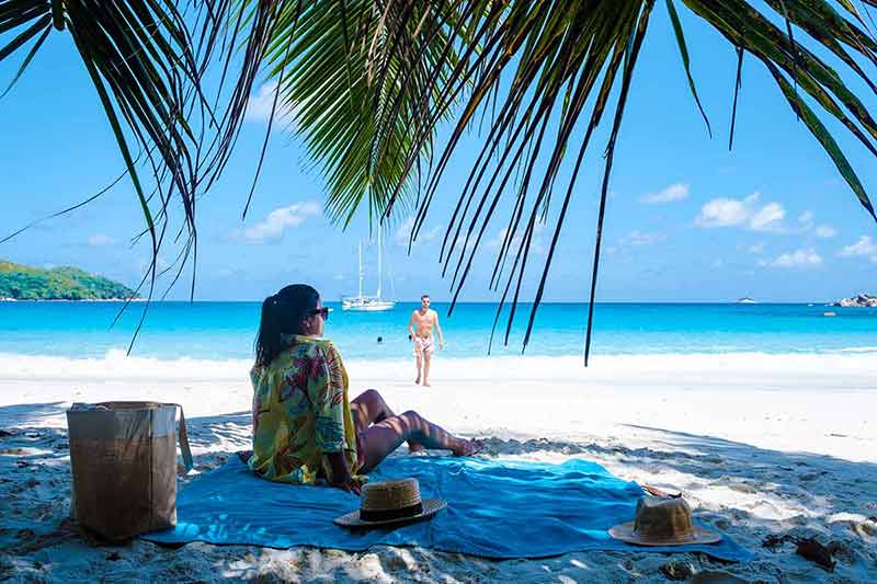 top 10 beaches in seychelles woman sitting on a towel under a palm tree on white sand