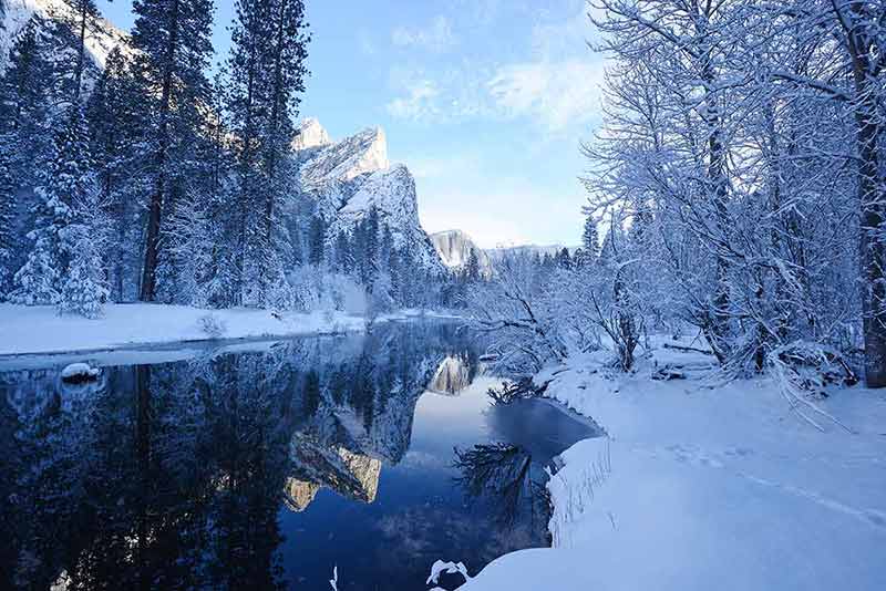 top national parks in california snow-covered mountains and trees reflected in a lake