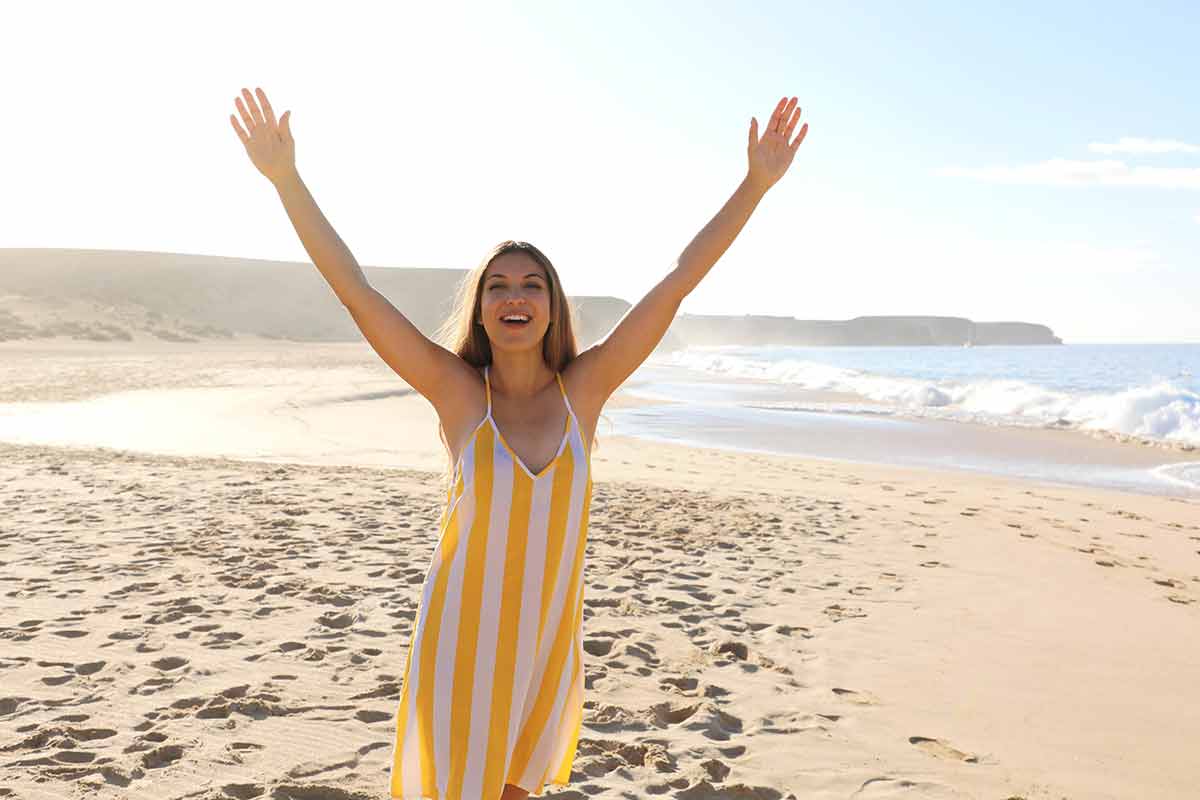 top things to do in lanzarote shot of a beautiful smiling woman with raised arms on Lanzarote sand beach in summer dress