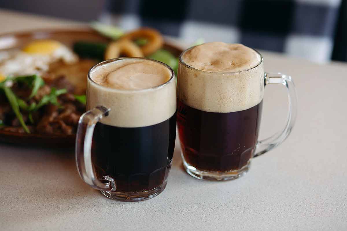 traditional german alcoholic drinks Two big glass cups full of foamy cold beer standing on light smooth table surface in restaurant or pub. Big plate with delicious appetizers like potato puncakes and fried eggs standing on background.