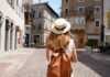 The best travel backpacks for women that frequent travellers swear by young woman wearing a straw hat and tan backpack walking through a European town