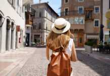 The best travel backpacks for women that frequent travellers swear by young woman wearing a straw hat and tan backpack walking through a European town