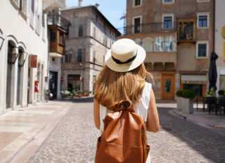 The best travel backpacks for women that frequent travellers swear by young woman wearing a straw hat and tan backpack walking through a European town