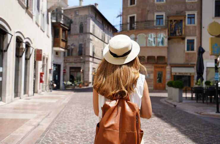 The best travel backpacks for women that frequent travellers swear by young woman wearing a straw hat and tan backpack walking through a European town