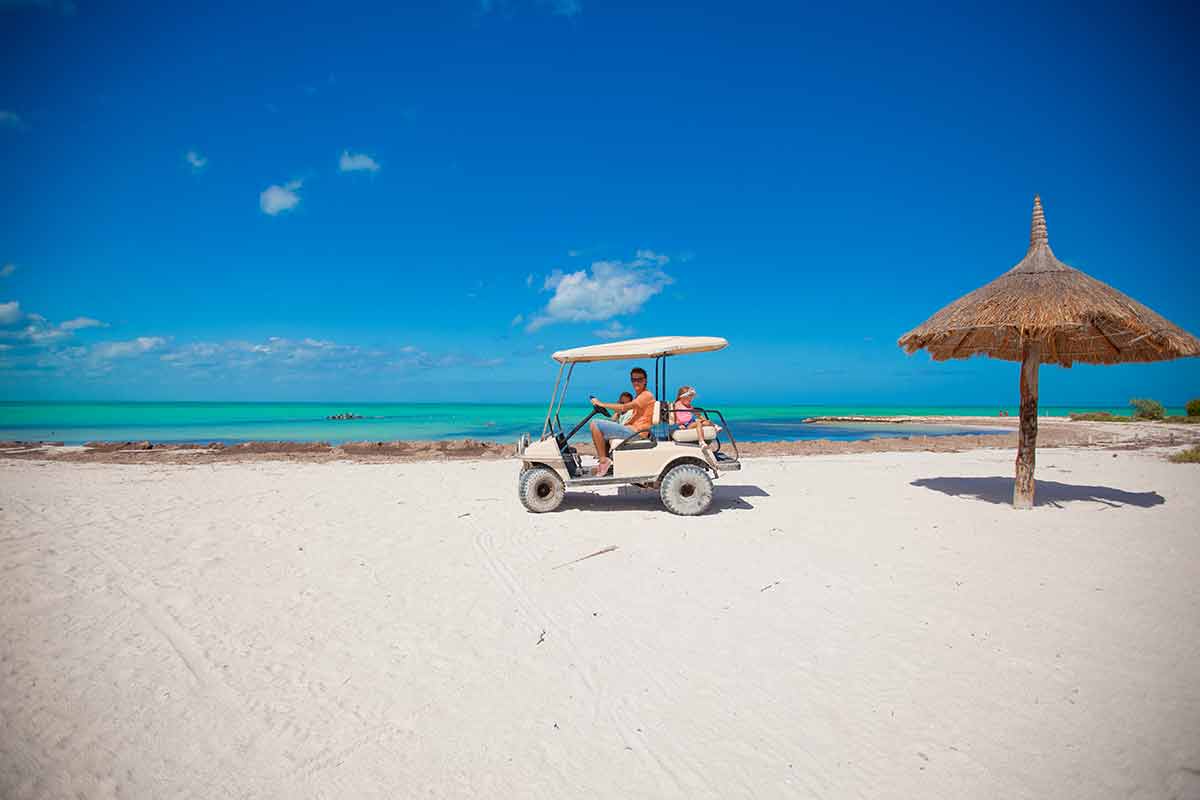 travel to cancun with kids Dad and little daughters driving golf cart on tropical beach