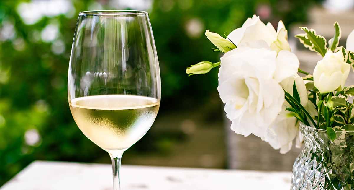 White Wine and vase of white flowers with blurred vines in the background