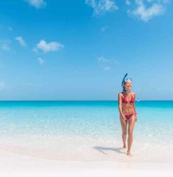 beautiful woman in red bikini wearing a snorkel walking out of the blue ocean in turks caicos