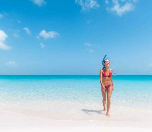 beautiful woman in red bikini wearing a snorkel walking out of the blue ocean in turks caicos