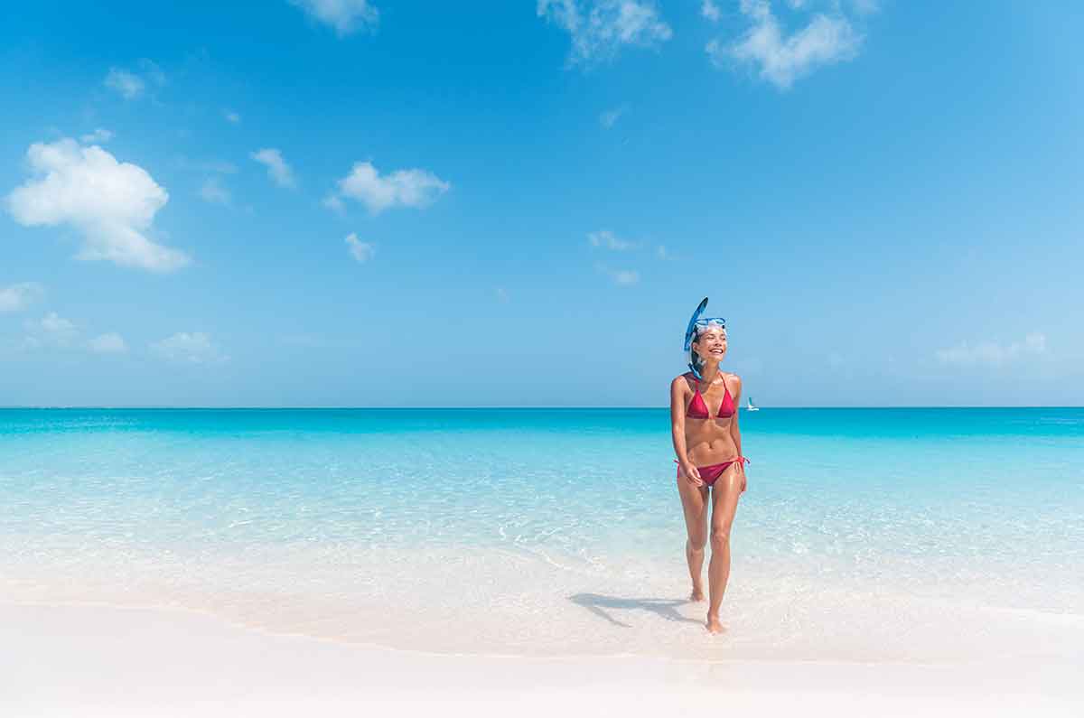 beautiful woman in red bikini wearing a snorkel walking out of the blue ocean in turks caicos