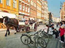 horse and buggy driving through the old town and people sitting at a bus stop