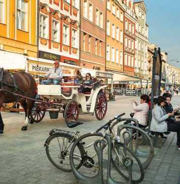 horse and buggy driving through the old town and people sitting at a bus stop
