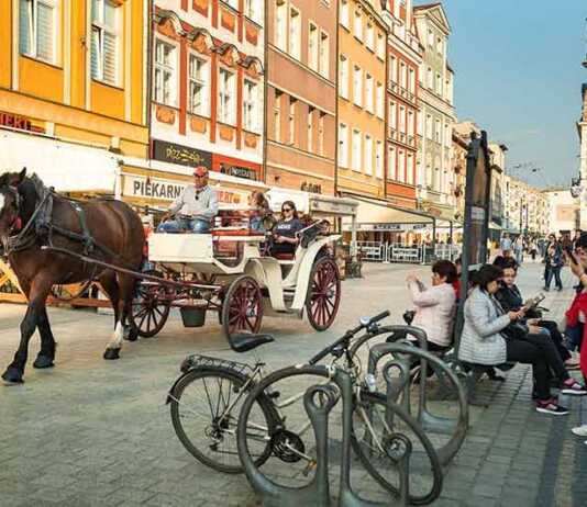 horse and buggy driving through the old town and people sitting at a bus stop