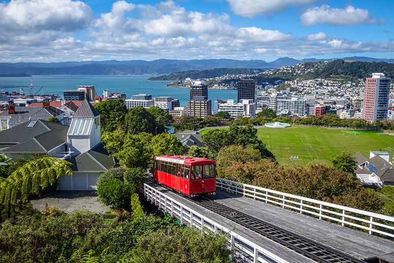 red cable car ascending a hill with city and harbour in the background