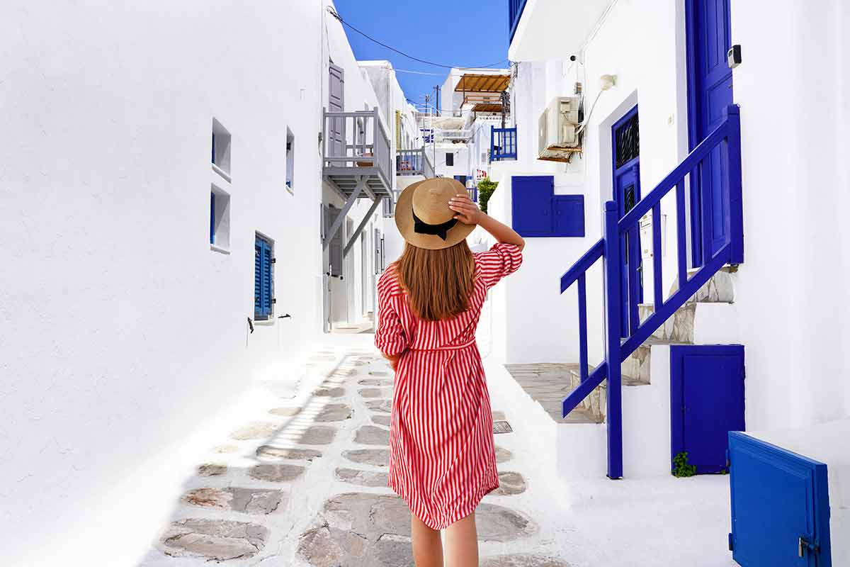 what are the best beaches in mykonos girl in red and white striped dress and hat walking through white-washed alley