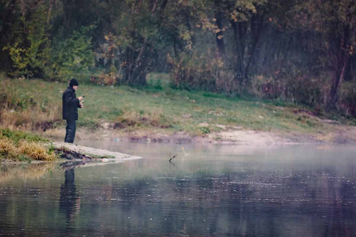 Fisherman In Blur On The Shore Of A River Lake