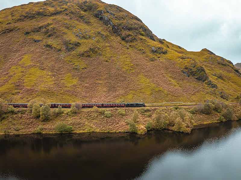 Steam Train In Scotland Passing By A Loch In The Highlands