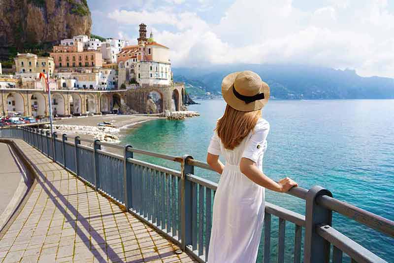 what is the best time to visit italy Back view of beautiful fashion girl enjoying view of Atrani village on Amalfi Coast.