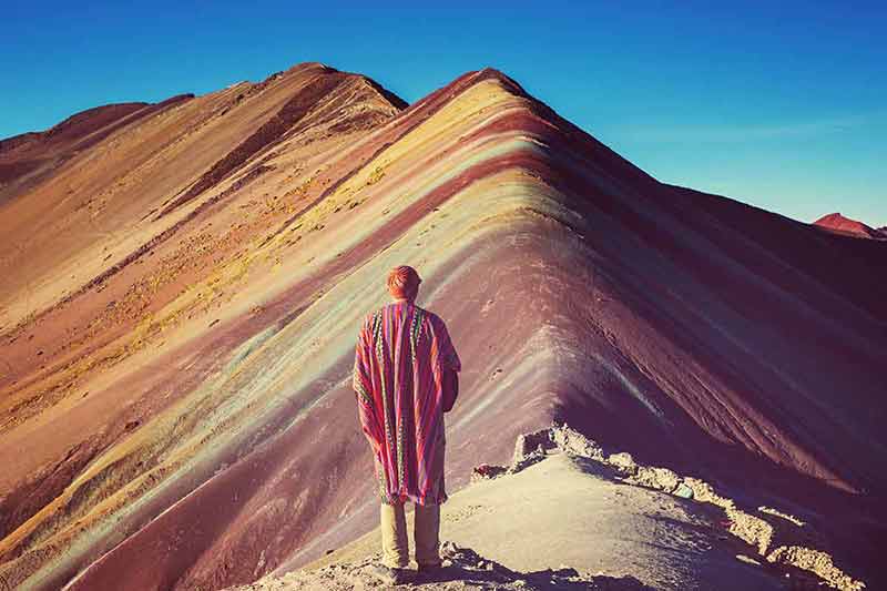 what is the best time to visit peru man wearing a poncho staring at themulticoloured mountain