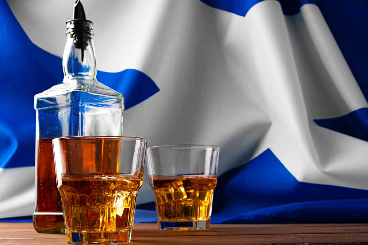 bottle and two glasses of whisky with Scottish flag in background
