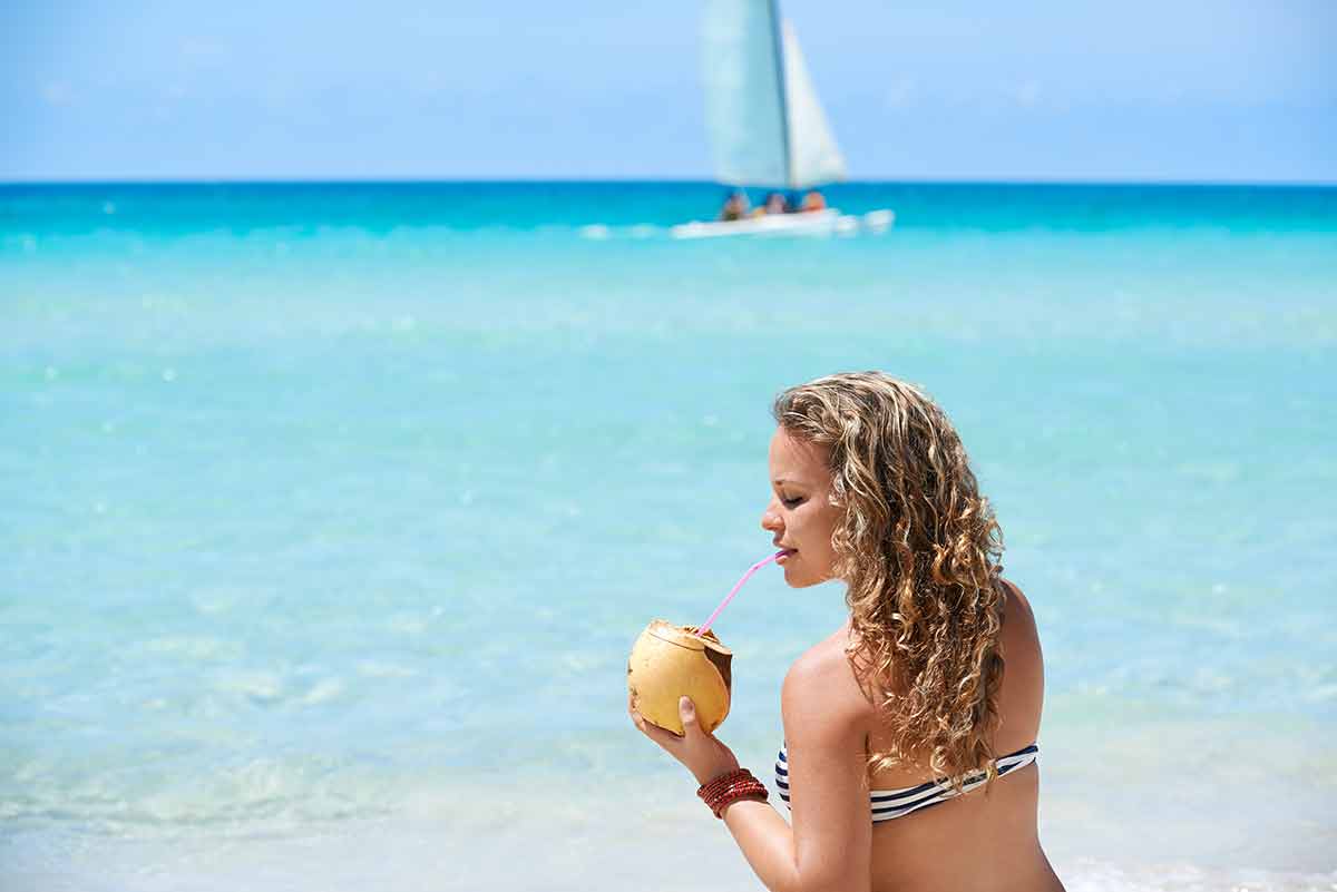 when's the best time to visit cuba Varadero girl drinking cocktail in a coconut and sitting on sand