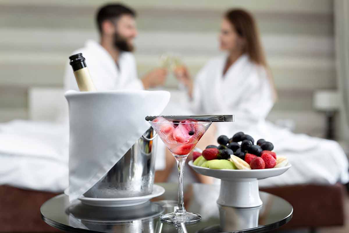 Romantic dinner in the hotel of berries and fruits for a young couple who drinks champagne in bed.