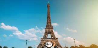 Rear View Of A Woman Tourist In Sun Hat Standing In Front Of Eiffel Tower