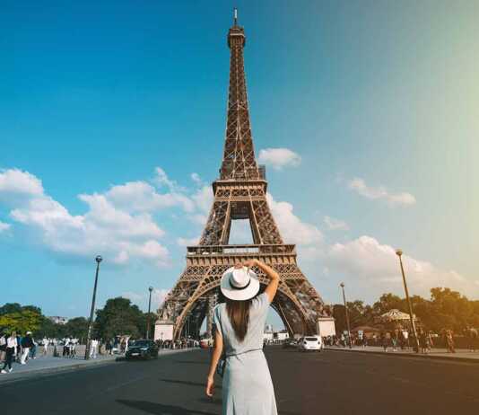 Rear View Of A Woman Tourist In Sun Hat Standing In Front Of Eiffel Tower