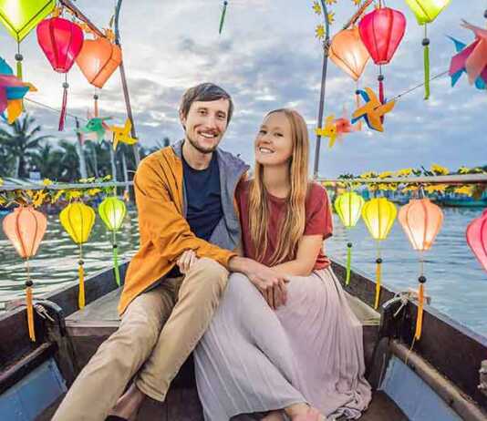 Happy couple of travelers ride a national boat on background of Hoi An ancient town, Vietnam.