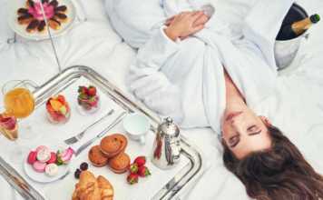 where to stay in los angeles as a tourist an attractive young woman in a bathrobe enjoying a luxurious breakfast in her room.