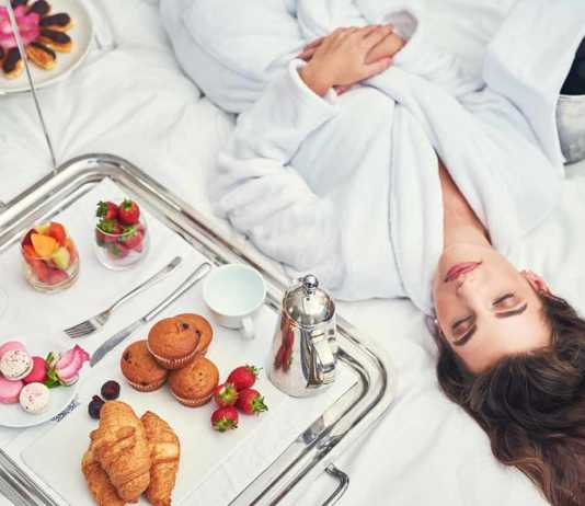where to stay in los angeles as a tourist an attractive young woman in a bathrobe enjoying a luxurious breakfast in her room.