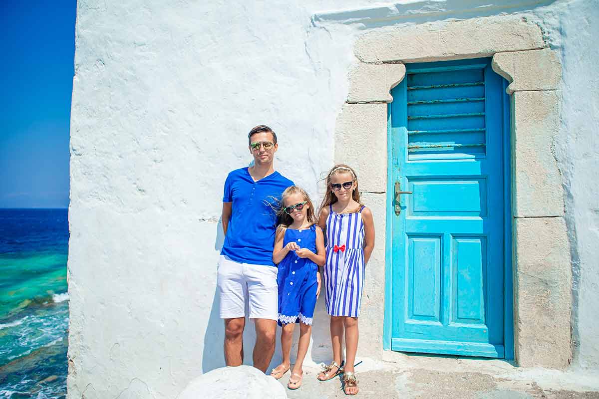 where to stay in mykonos with no car dad and two girls standing next to a blue door.